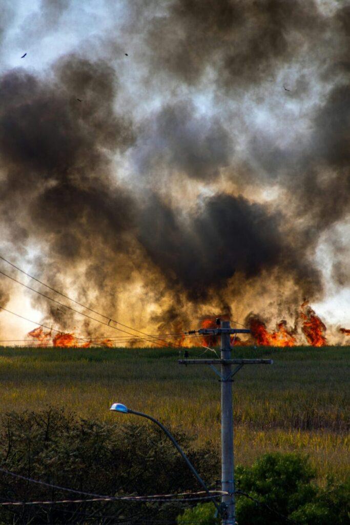 A fire spreading across a field nearing a telephone pole