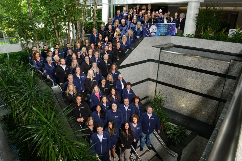 A large group of attorneys and staff of Capehart Scatchard standing on a stairwell with a banner for the firm's 150th Anniversary.