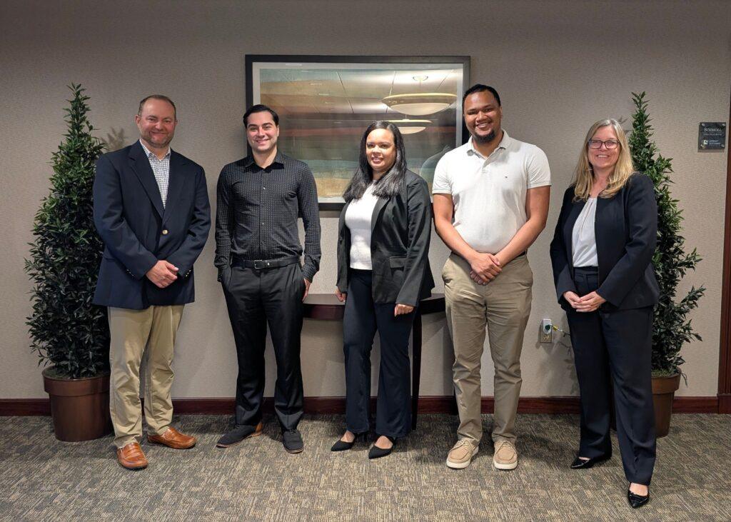 5 smiling individuals in business attire standing side by side of one another in law firm lobby