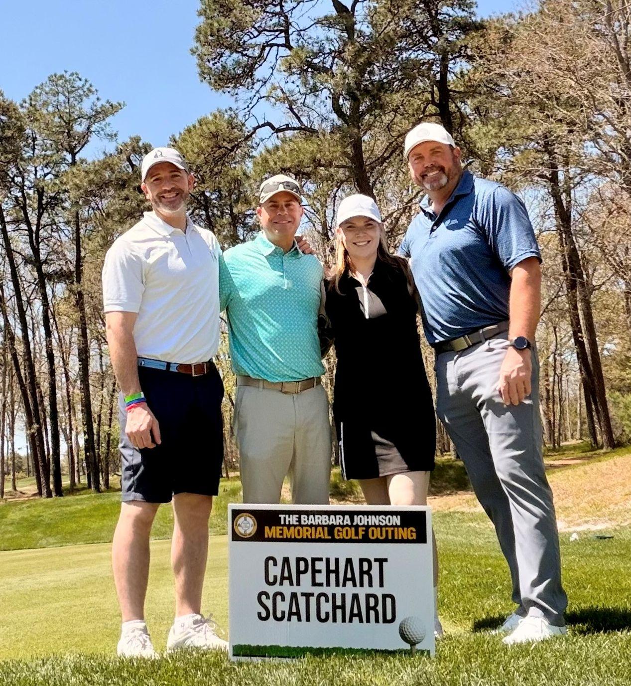 Picture at Golf Course in front of sign saying the name of Capehart Scatchard with a team of golfers