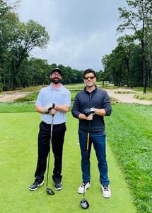 Two gentlemen standing on a golf course each holding a golf club and smiling